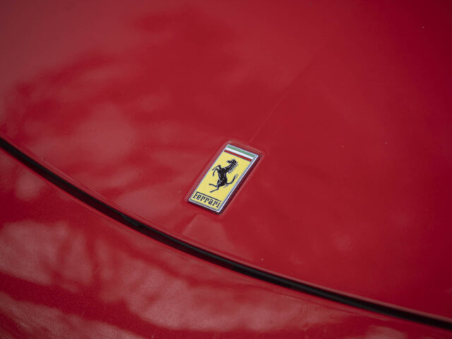 Close-up van de motorkap van een rode auto met een Ferrari 458 Italia-embleem met een steigerend paard.