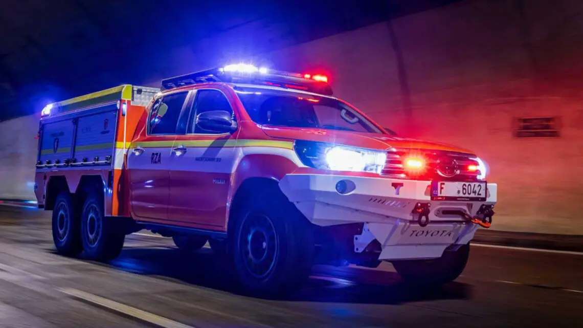 Een elektrische auto met knipperende rode en blauwe lichten rijdt door een tunnel en doet dienst als brandweer- en reddingsvoertuig.