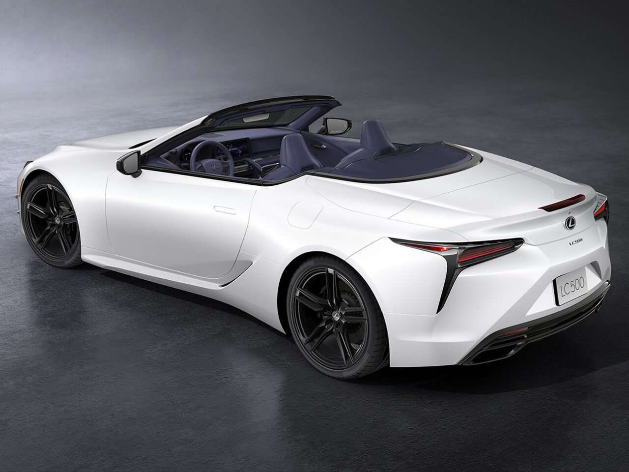 Een witte Lexus LC cabrioletsportwagen met een strak ontwerp, met de bovenkant naar beneden en naar links gericht op een donker, gepolijst oppervlak.