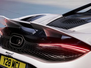 Close-up van de achterkant van een witte McLaren 750S-supercar, met het aerodynamische ontwerp, de dubbele achtervleugels, het ingewikkelde grillepatroon en de verlichte achterlichten. Op het kenteken staat "Y28 MCL".