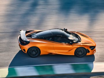 Een oranje McLaren 750S-sportwagen rijdt op een racecircuit, vanuit een hoge hoek bekeken. De auto is strak met aerodynamische lijnen en het circuit is voorzien van groene en witte stoepranden.