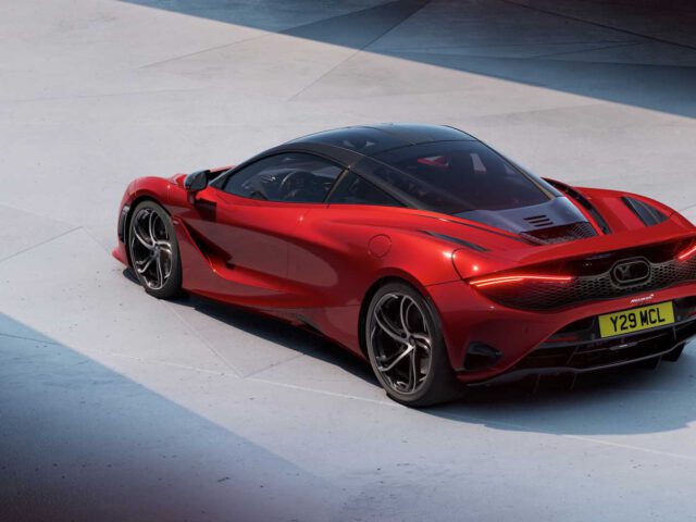 Op een betonnen ondergrond staat een rode McLaren 750S met een strak design en aerodynamische kenmerken geparkeerd. Op het kenteken staat "Y29 MCL".