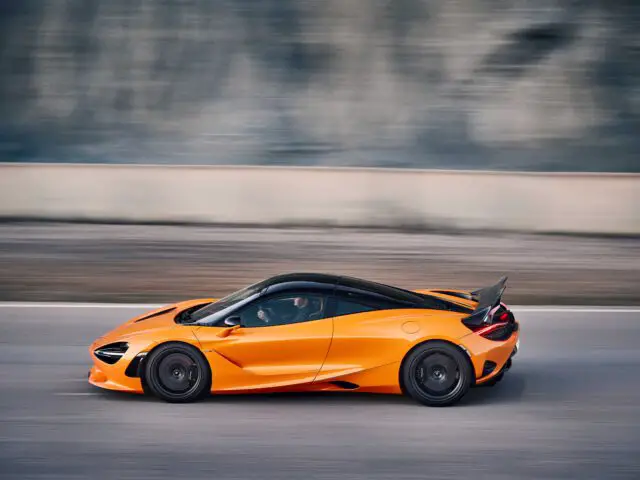 Een oranje McLaren 750S-sportwagen met zwarte accenten die over het circuit snelt, vastgelegd in een zijprofiel.