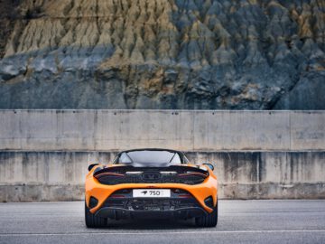 Achteraanzicht van een McLaren 750S, een oranje sportwagen geparkeerd voor een rotsachtige klif. Op het kenteken van de auto staat "750S.