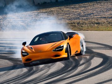 Een feloranje McLaren 750S voert een driftmanoeuvre uit op een circuit, waarbij rook uit de achterbanden komt, terwijl de bandensporen zichtbaar zijn op het asfalt.