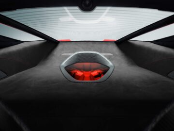 Uitzicht op het interieur van de McLaren 750S met de motor met een rood onderdeel, gezien door de achterruit. Het interieur is voorzien van donkere bekleding en koolstofvezelelementen.