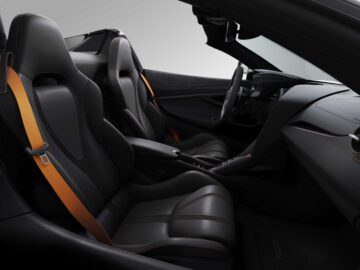 Interieur van de McLaren 750S met strakke zwartleren stoelen met oranje veiligheidsgordels, een minimalistisch dashboard en een sportief stuur.