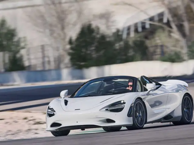 Een witte sportwagen McLaren 750S die op een racecircuit rijdt met een onscherpe achtergrond, inclusief bomen en een betonnen barrière.