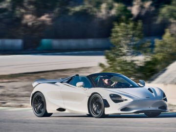 Een witte McLaren 750S sportwagen met cabriokap rijdt op een racecircuit, omgeven door wazig groen op de achtergrond.