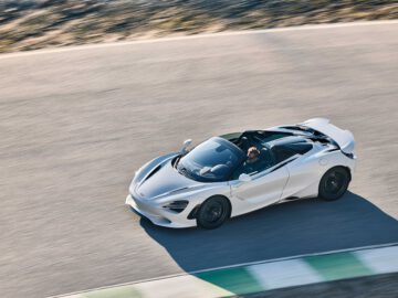 Een McLaren 750S convertible sportwagen met een strak design rijdt op een racecircuit met groen-witte stoepranden.