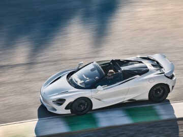 Een witte McLaren 750S-sportwagen rijdt op een circuit, vastgelegd vanuit een hoek van bovenaf. De auto rijdt met hoge snelheid, waarbij een wazige omgeving beweging aangeeft.