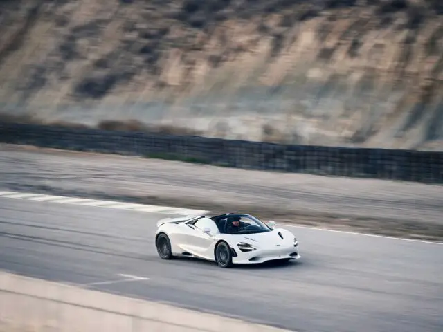 Een witte McLaren 750S rijdt met hoge snelheid op een racecircuit nabij een bergachtig gebied.