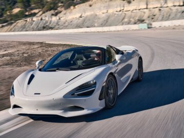 Een strakke witte McLaren 750S converteerbare sportwagen glijdt moeiteloos over een bochtige bergweg onder een heldere hemel.