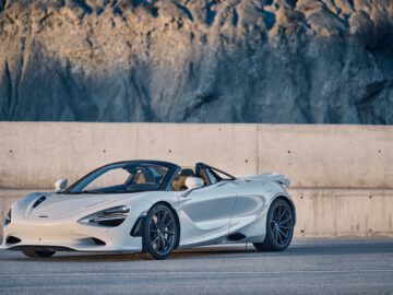 Een strakke witte McLaren 750S converteerbare sportwagen staat geparkeerd op een verhard oppervlak voor een rotsachtige achtergrond.