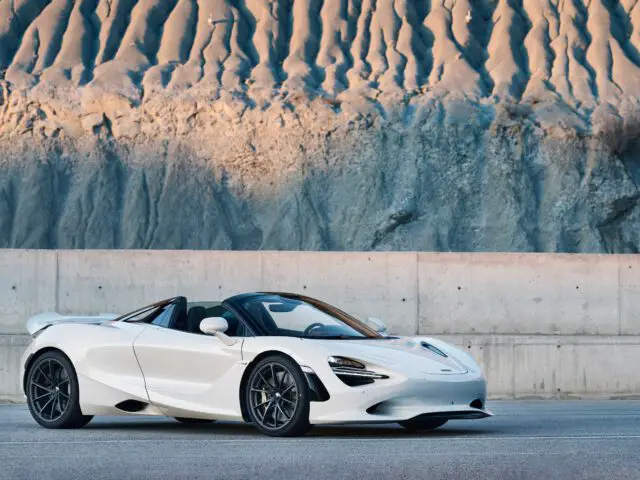 Een witte McLaren 750S met het dak open staat geparkeerd voor een ruige klif en een betonnen barrière.