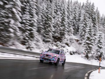 Een gecamoufleerde MINI Countryman rijdt over een bochtige, besneeuwde bergweg met aan weerszijden pijnbomen.