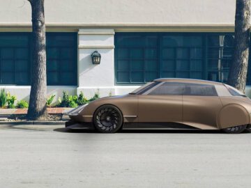 Een matbruine futuristische DS-auto staat geparkeerd in een straat voor een beige en blauw gebouw met grote ramen en lantaarnvormige lampen.