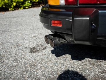 Close-up van de achterbumper en uitlaatpijpen van een Porsche 930 geparkeerd op een grindoppervlak.