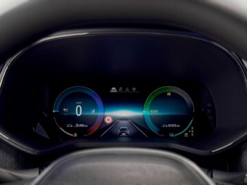 Close-up van het digitale dashboarddisplay van een Renault Clio met snelheid, batterijniveau en navigatie-informatie op een digitale weg. De snelheidsmeter geeft 0 km/u aan en de batterij-indicatoren staan op verschillende niveaus.