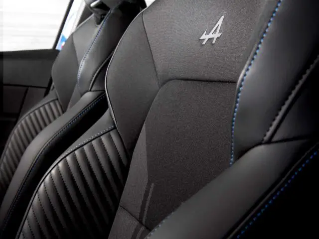 Close-up van het zwarte interieur van een Renault Clio met twee voorstoelen met blauwe stiksels en het nummer "4" geborduurd op de hoofdsteunen.