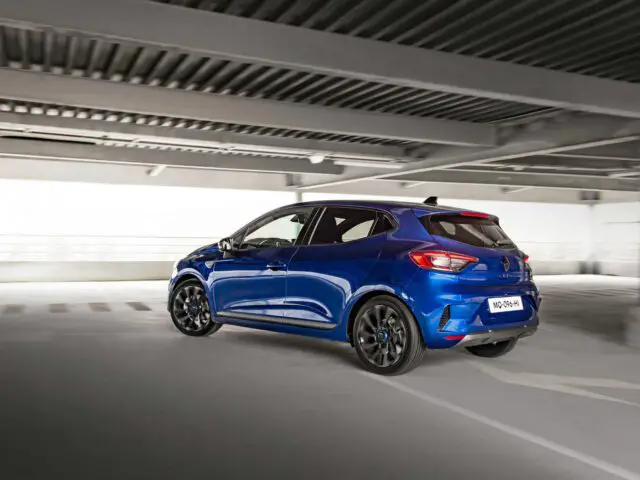 Een blauwe Renault Clio hatchback staat binnen geparkeerd in een parkeergarage met meerdere verdiepingen en betonnen balken erboven.