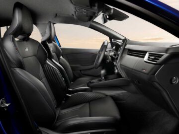 Een modern Renault Clio-interieur is voorzien van zwart lederen stoelen met blauwe stiksels, een handmatige versnellingspook en een strak dashboard met minimalistisch design. De scène baadt in natuurlijk licht.