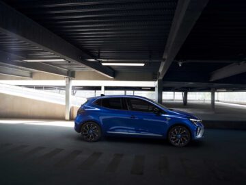 Een blauwe Renault Clio hatchback geparkeerd in een slecht verlichte parkeergarage met meerdere verdiepingen.