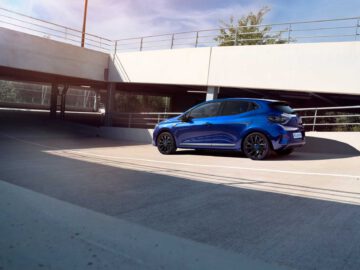 Een blauwe Renault Clio hatchback staat geparkeerd in een parkeergarage met meerdere verdiepingen, waar zonlicht schaduwen werpt.