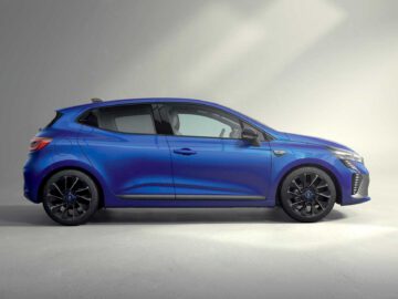 Een blauwe Renault Clio hatchback met zwarte wielen staat geparkeerd in een goed verlichte studio, vanaf de zijkant gezien.