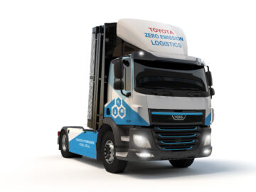 Een wit-blauwe semi-vrachtwagen met "Toyota Zero Emission Logistics" op de cabine geschreven. De vrachtwagen, voorzien van waterstofbrandstofceltechnologie, vertegenwoordigt de toekomst van duurzaam transport.