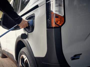 Een persoon steekt een oplaadkabel in de poort van een witte Ford E-Tourneo Courier met een zwart en oranje achterlicht.