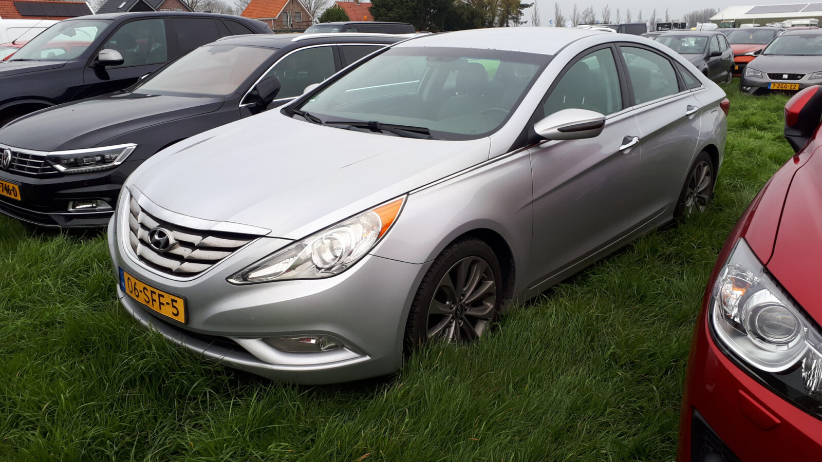 Een zilverkleurige Hyundai Sonata sedan staat tussen andere voertuigen op het gras geparkeerd.