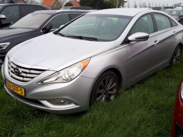 Een zilverkleurige Hyundai Sonata sedan staat tussen andere voertuigen op het gras geparkeerd.