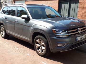 Een zilveren Volkswagen Atlas staat geparkeerd op een geplaveide straat voor rode bakstenen gebouwen.