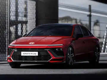 Een rode Hyundai Sonata N Line staat geparkeerd voor een hekwerk, wat het slanke voor- en zijprofiel van de Hyundai Sonata laat zien.