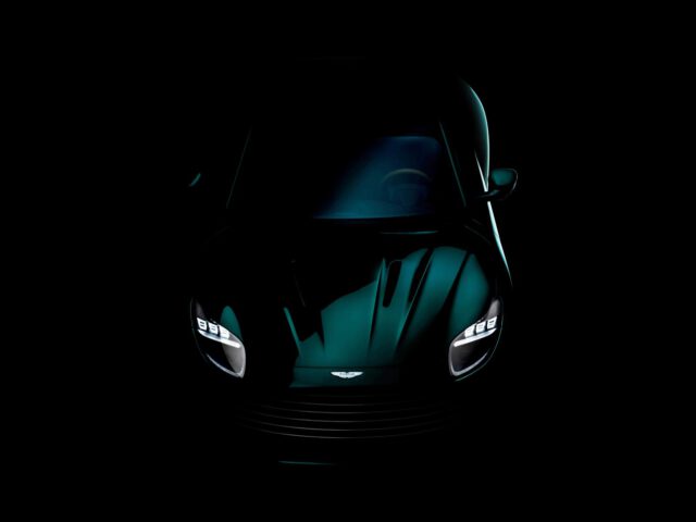 Een donker verlicht vooraanzicht van een Aston Martin-sportwagen met zichtbare LED-koplampen en een logo op de motorkap. De achtergrond is volledig zwart, wat het strakke design van de auto benadrukt.