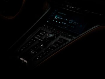 Een slecht verlichte binnenaanzicht van het dashboard van een Aston Martin-auto met een digitaal beeldscherm en verschillende bedieningsknoppen.