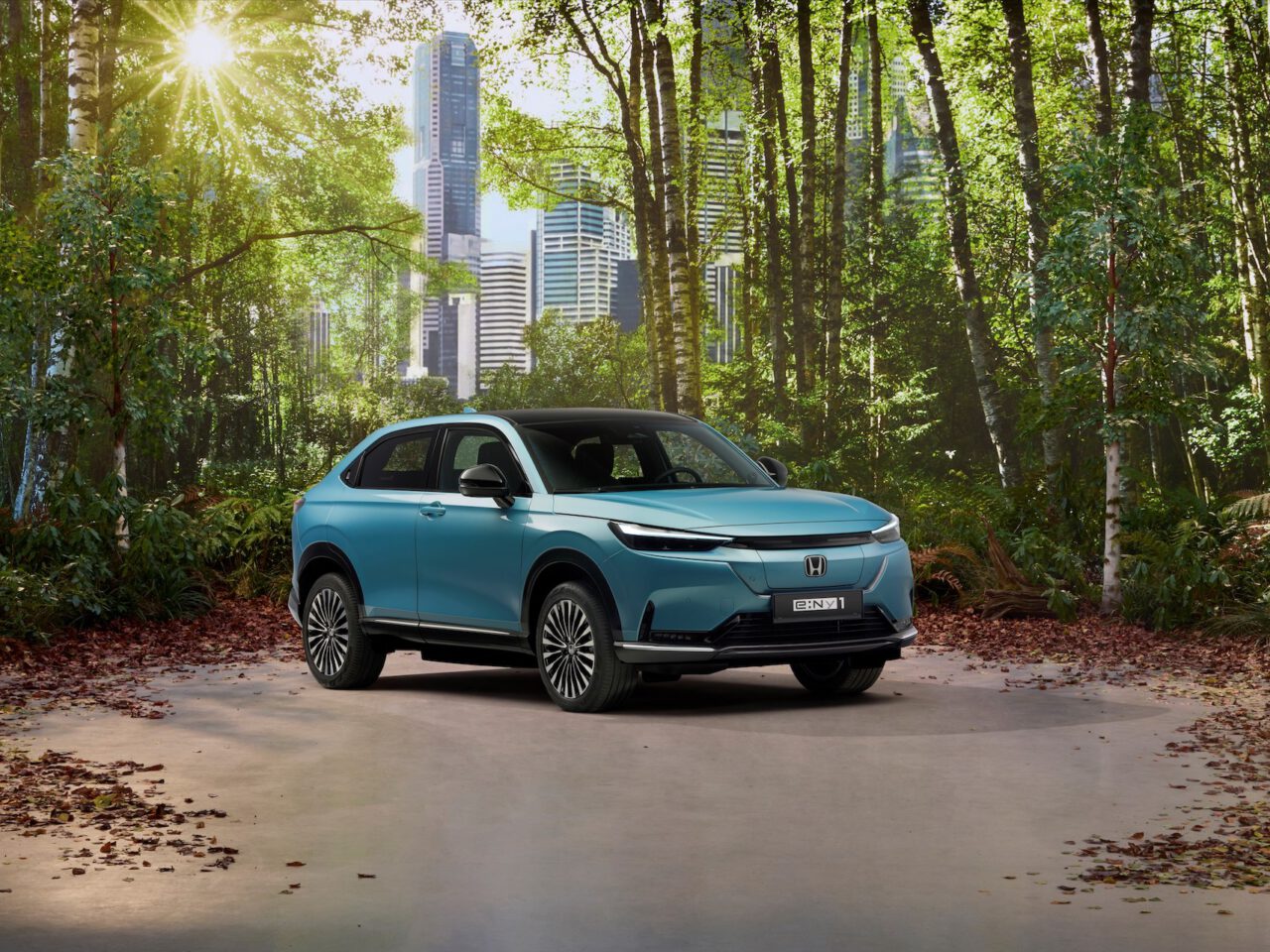 Een blauwe Honda e:Ny1 SUV staat geparkeerd op een pad in een bos met hoge stadsgebouwen zichtbaar op de achtergrond onder een felle zon.