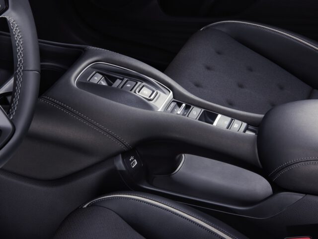 Close-up van het interieur van de Honda ZR-V, waarbij de middenconsole en stoelen centraal staan. De console bevat een versnellingspook en verschillende bedieningsknoppen, met stiksels op de stoelen en de omliggende gebieden.