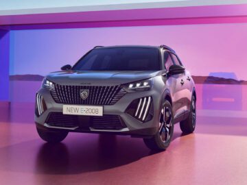 Een grijze Peugeot 2008 E-2008 wordt weergegeven op een gepolijst oppervlak met een roze en paarse achtergrond, waardoor het voor- en zijprofiel goed zichtbaar zijn.