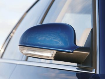 Close-up van de zijspiegel van een blauwe Volkswagen Passat met de lucht weerspiegeld op het oppervlak. De spiegel is voorzien van een geïntegreerd richtingaanwijzerlicht.
