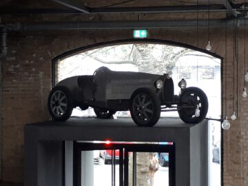 Een klassieke Remise zwarte vintage auto wordt tentoongesteld op een verhoogd platform in een kamer in industriële stijl met bakstenen muren en een gebogen raam op de achtergrond.