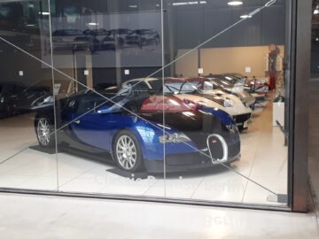 Een reeks luxe auto's, waaronder een blauwe Bugatti, is te zien in de Classic Remise-showroom met grote glazen ramen.