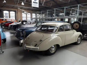 Een collectie oldtimers wordt tentoongesteld in de Classic Remise, een ruime overdekte showroom met grote ramen en metalen planken erboven.