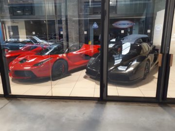 Een showroomdisplay bij Classic Remise toont twee supercars, een rode en een zwarte, elegant gepresenteerd achter glazen deuren.