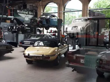 Klassieke Remise oldtimerwerkplaats met meerdere klassieke auto's die binnenshuis worden gerepareerd op liften en werkstations.