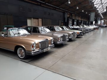 Een rij klassieke oldtimers opgesteld in de industriële showroom van Classic Remise, met hoge plafonds en grote ramen.