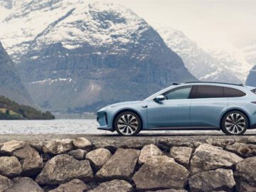 Een blauwe Nio ET5-toerwagen staat geparkeerd op een rotsachtige ondergrond met op de achtergrond besneeuwde bergen en een meer.