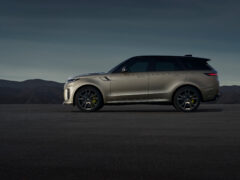 Een zijaanzicht van een metallic grijze Range Rover Sport SV met donkere wielen, geparkeerd op een open weg tegen een achtergrond van bergen en een donkerblauwe lucht.
