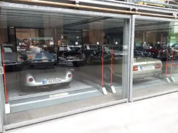 Verschillende oldtimers staan geparkeerd in een inpandige autogarage, zichtbaar door de glazen deuren van Classic Remise.